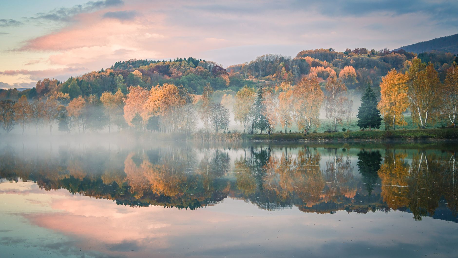 Tranquil autumn scene with colorful trees reflecting in a misty lake at dusk.