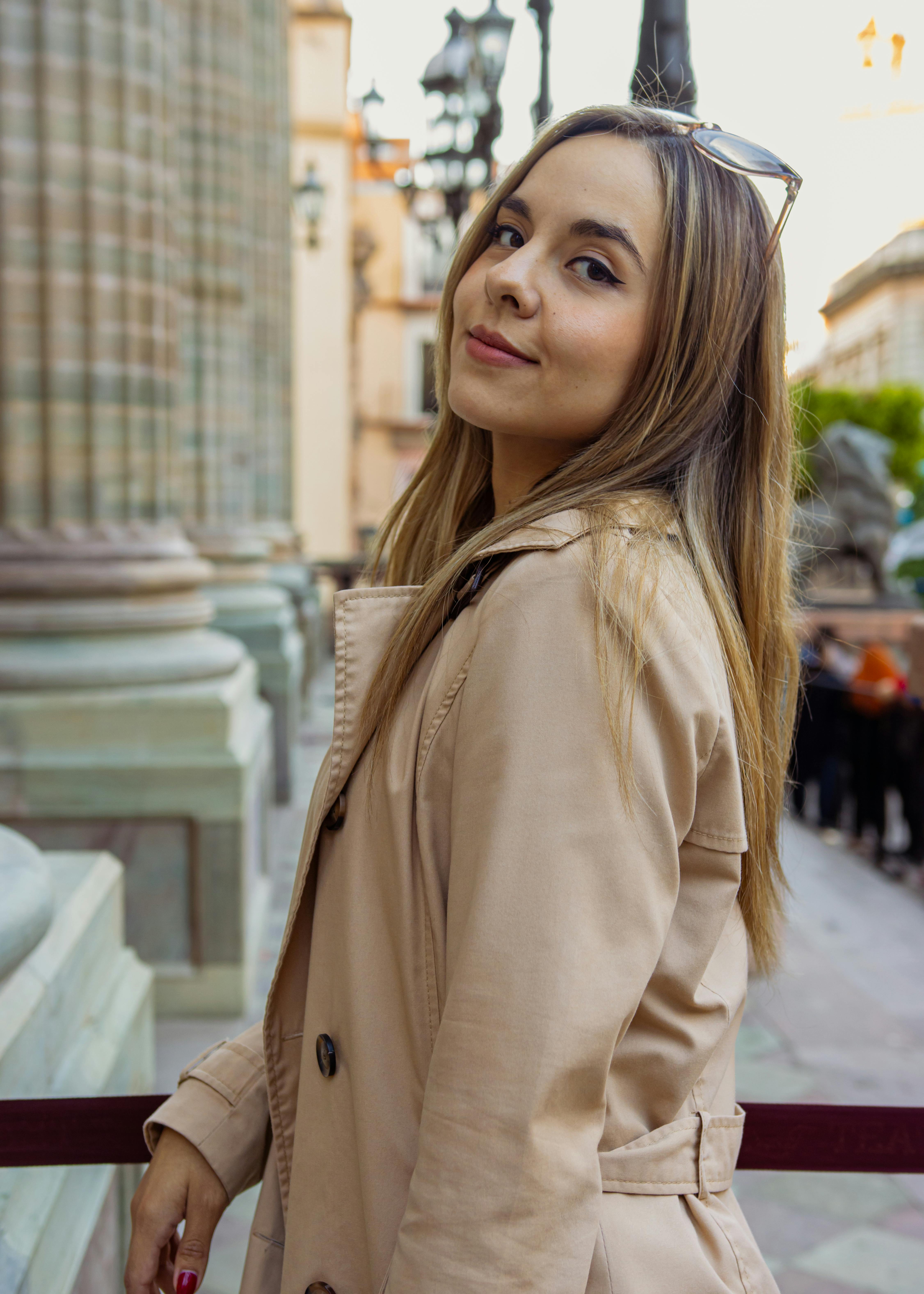 common:alt.prefix Güneşli bir günde bina sütunlarının yakınında poz veren paltolu kendine güvenen kadın. common:alt.postfix