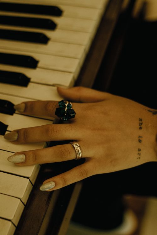 Free Close-up of a hand with rings and tattoo on piano keys, dim lighting. Stock Photo