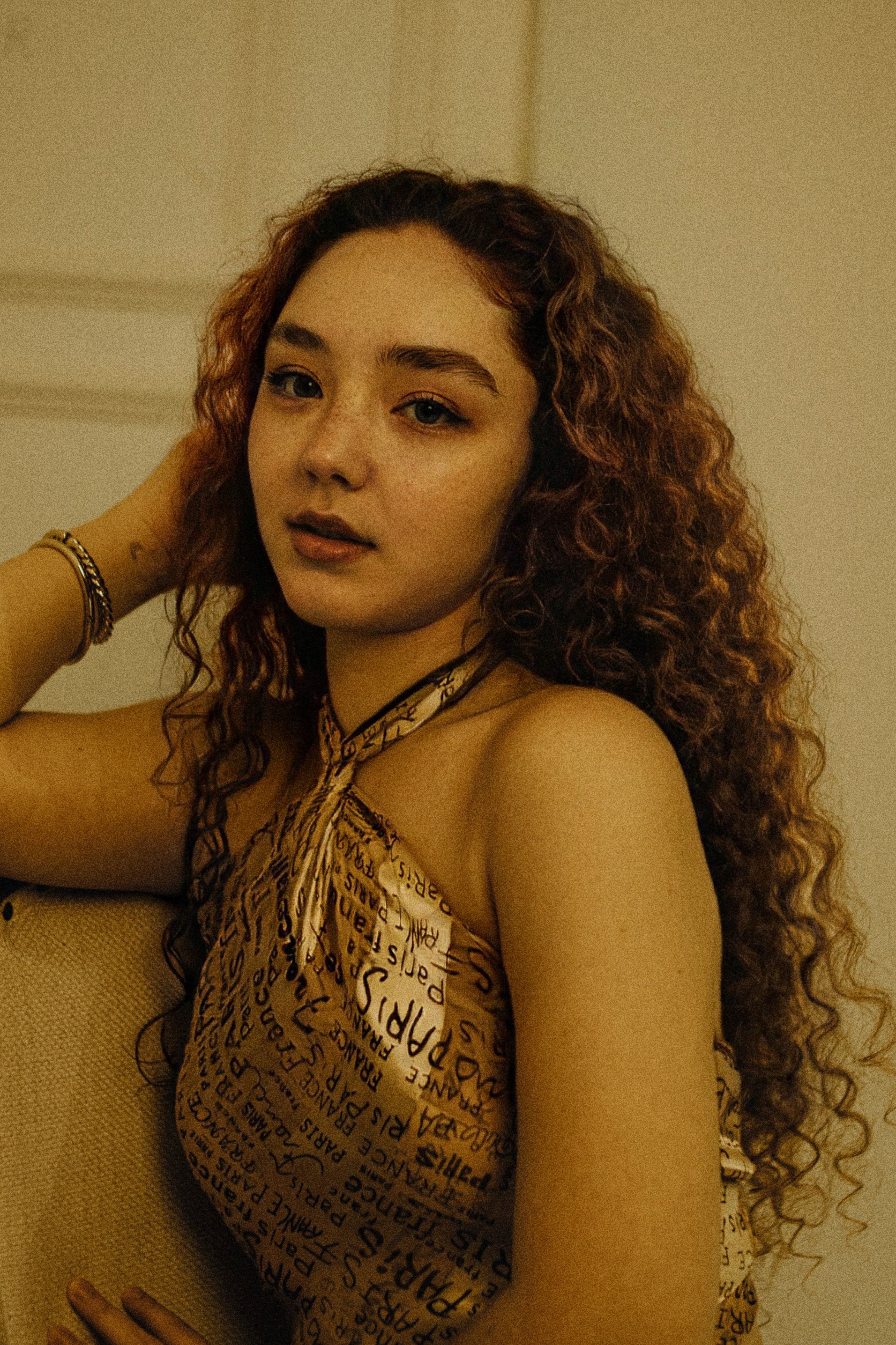 Stylish young woman with curly hair in a warm-toned indoor setting.