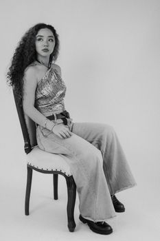 Elegant woman in trendy fashion sitting on a chair in a black and white portrait.