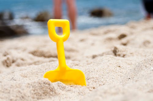 Желтая лопата, наполовину похороненная на песке у океана