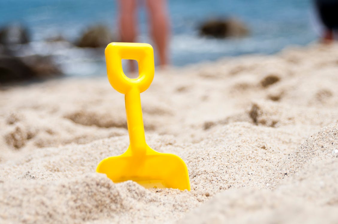 Yellow Shovel Half Buried on Sand Near the Ocean