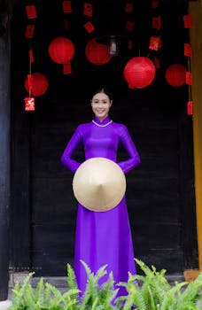 Elegant Vietnamese woman in purple Ao Dai holding conical hat, standing amidst red lanterns in Hội An.