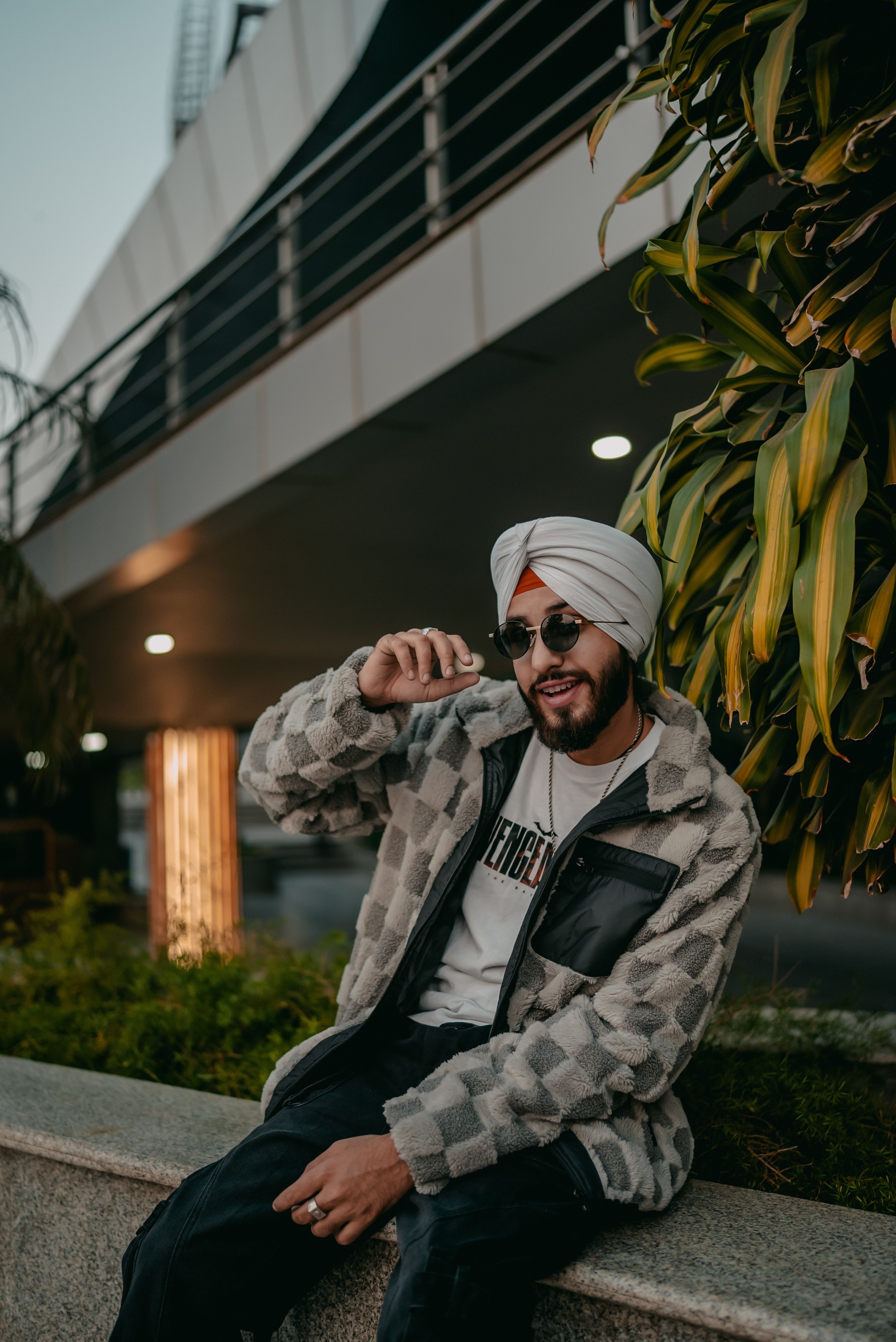 A fashionable young man wearing sunglasses and a turban sitting outside, exuding a vibrant urban vibe.