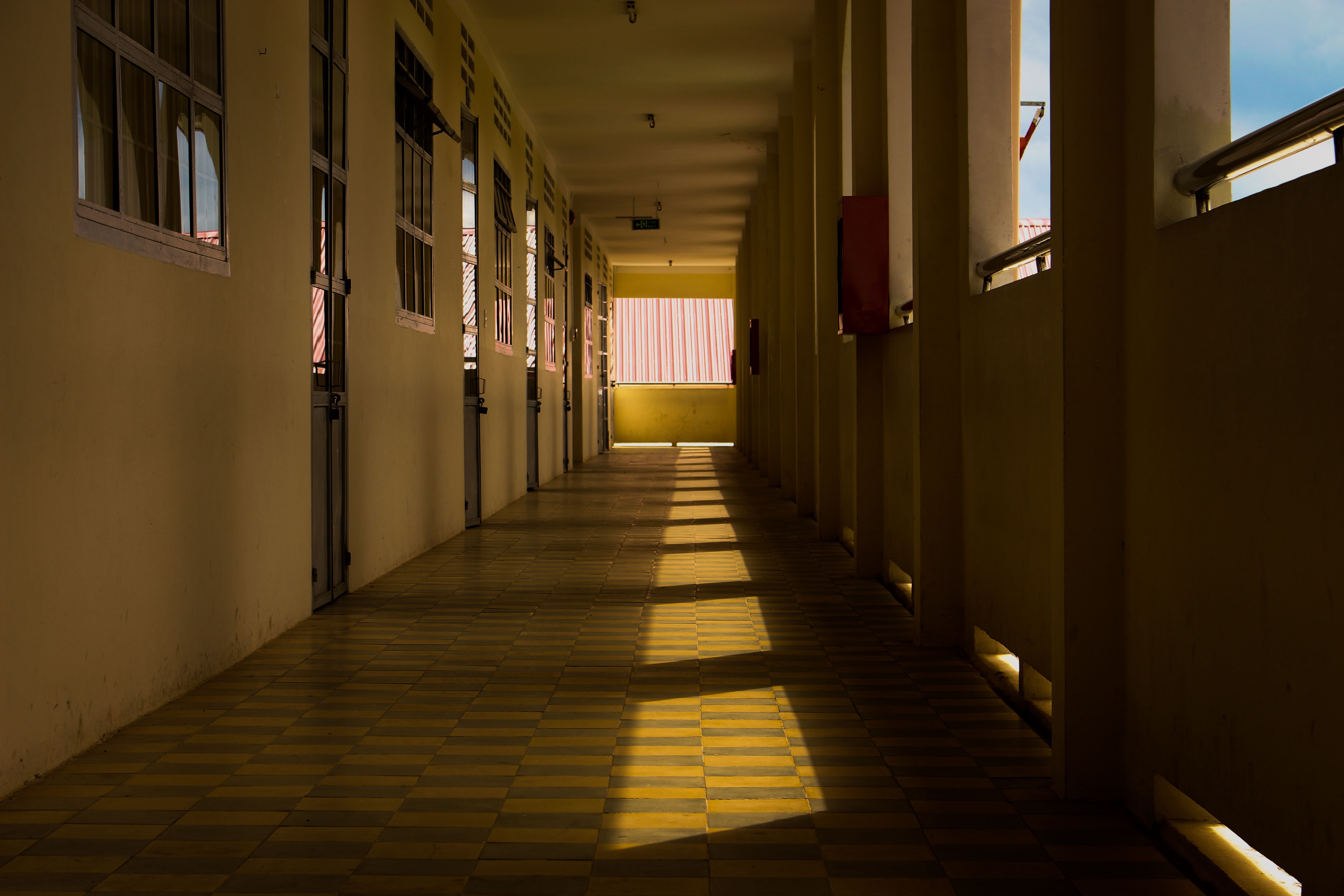 Corridor in a school building with sunlight casting shadows through windows, creating a patterned floor.
