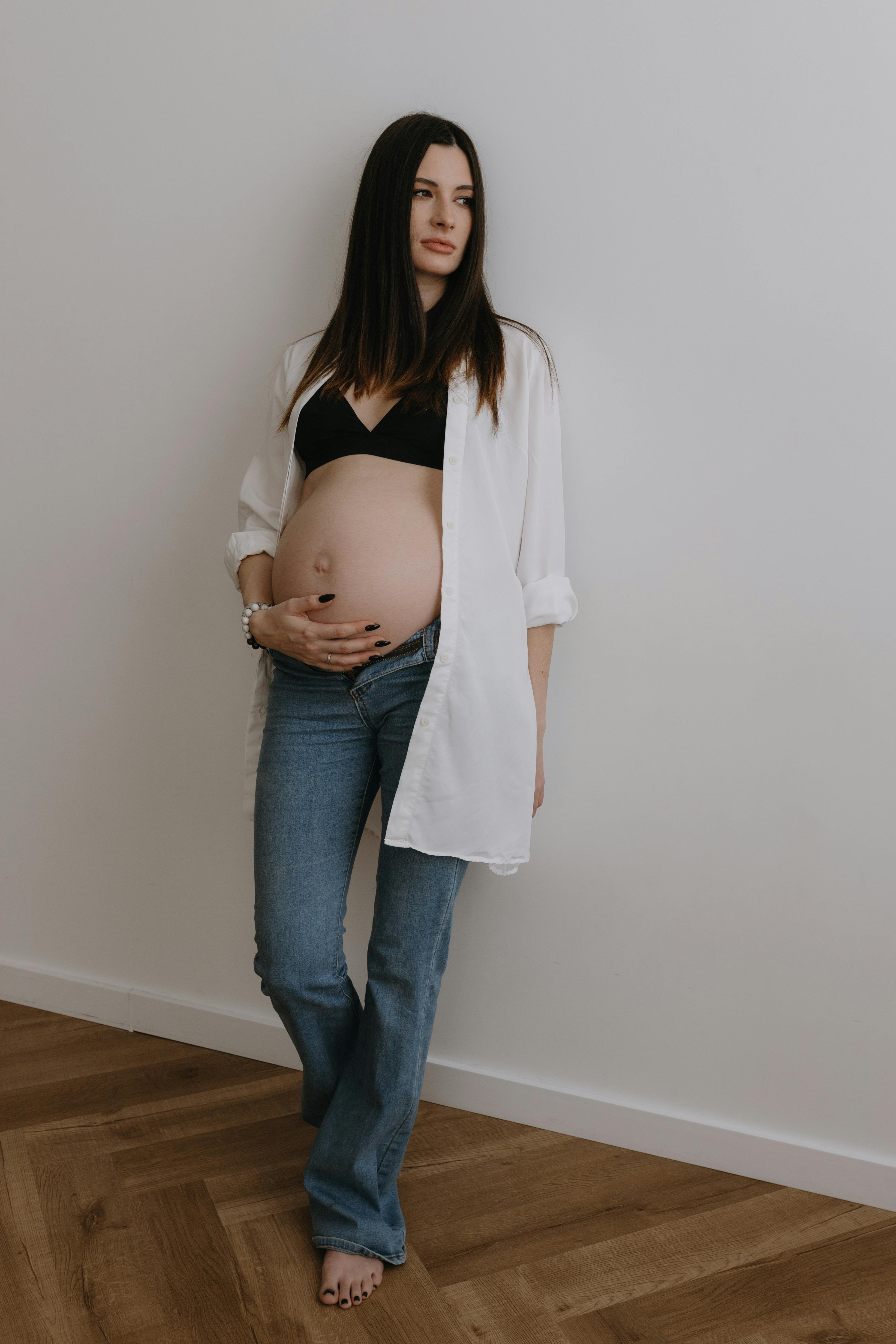 Pregnant woman relaxing indoors, wearing casual clothes, enjoying a serene moment.