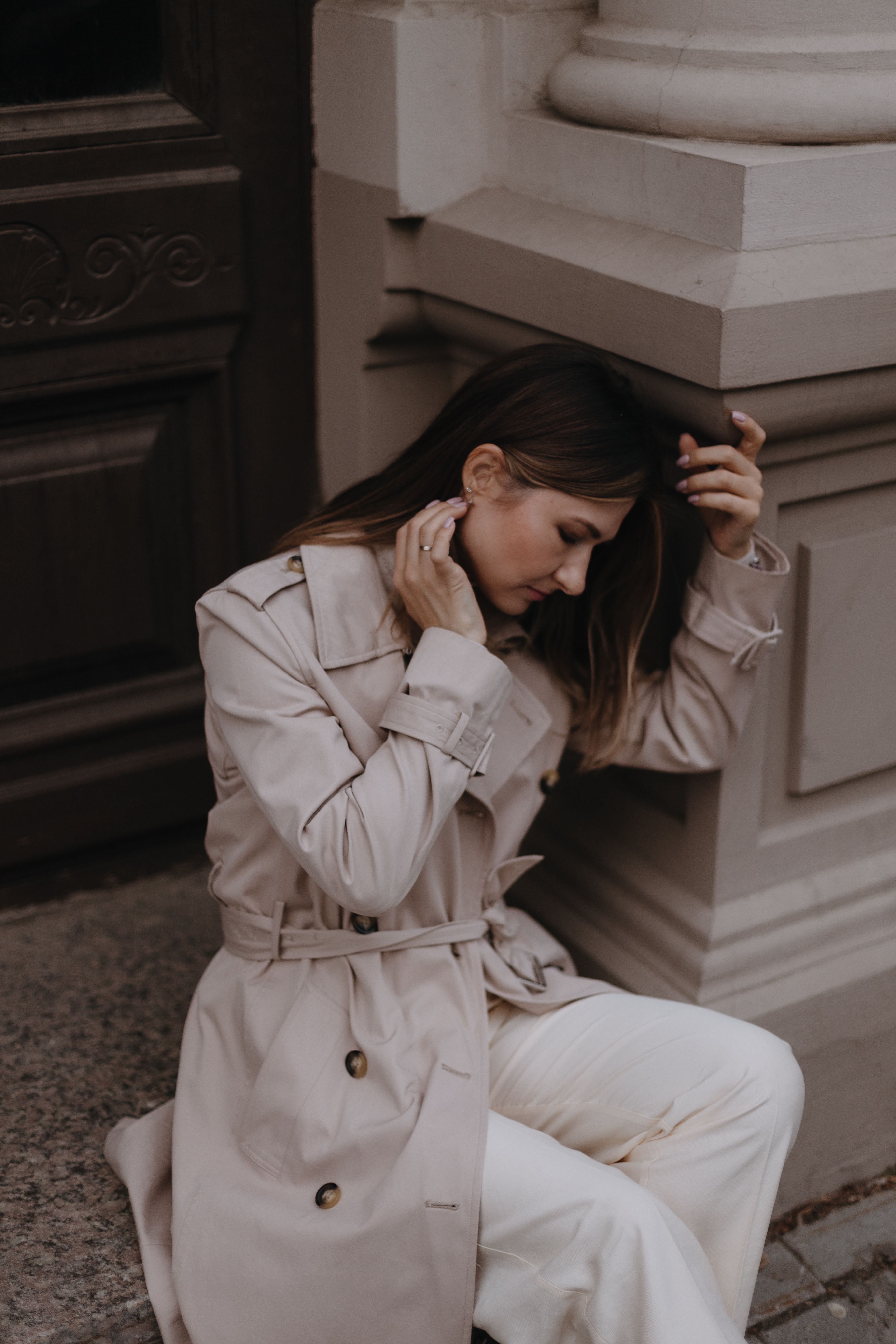 Thoughtful Woman Sitting Outdoors in Trench Coat · Free Stock Photo