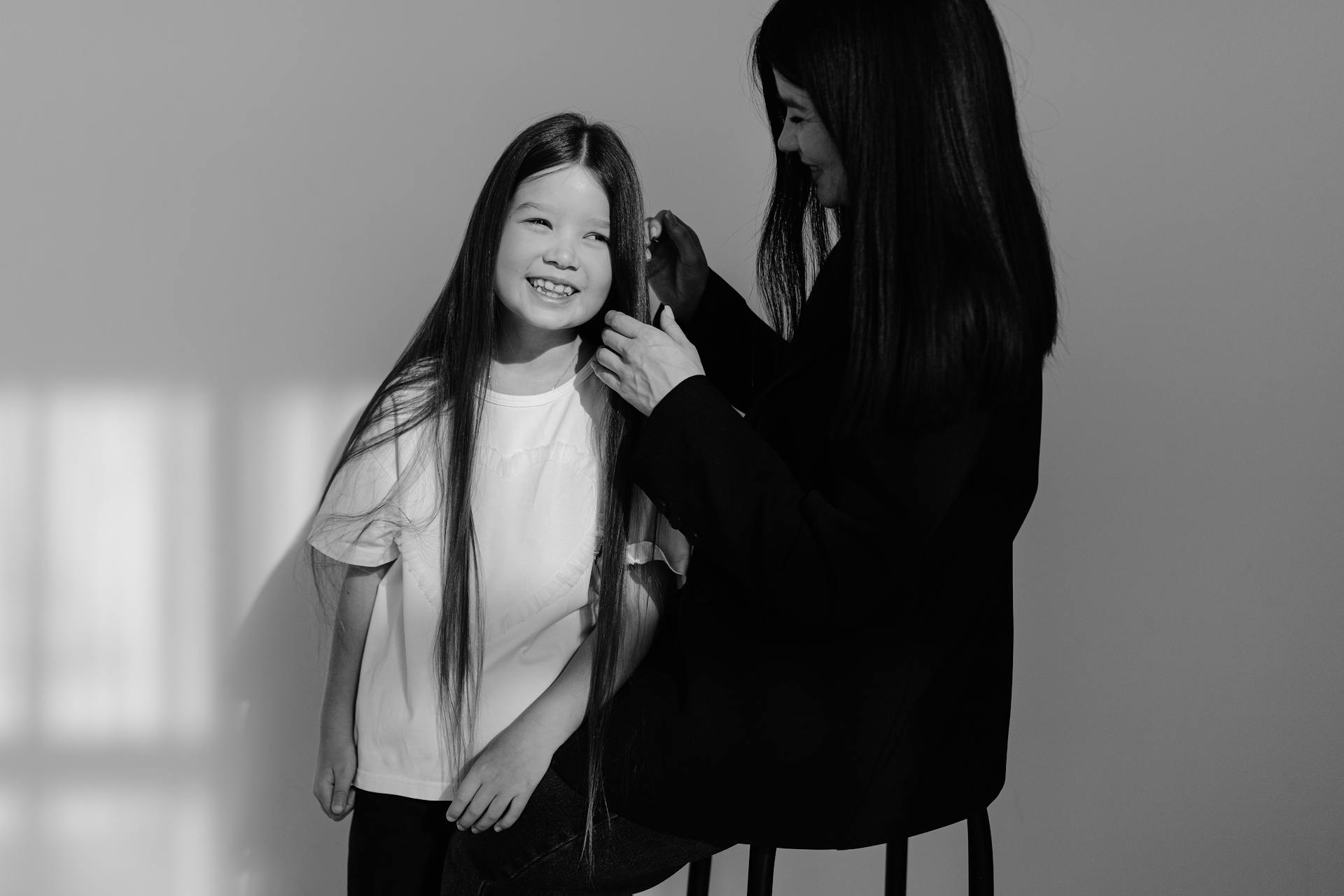 A mother lovingly brushes her daughter's hair in soft natural light.