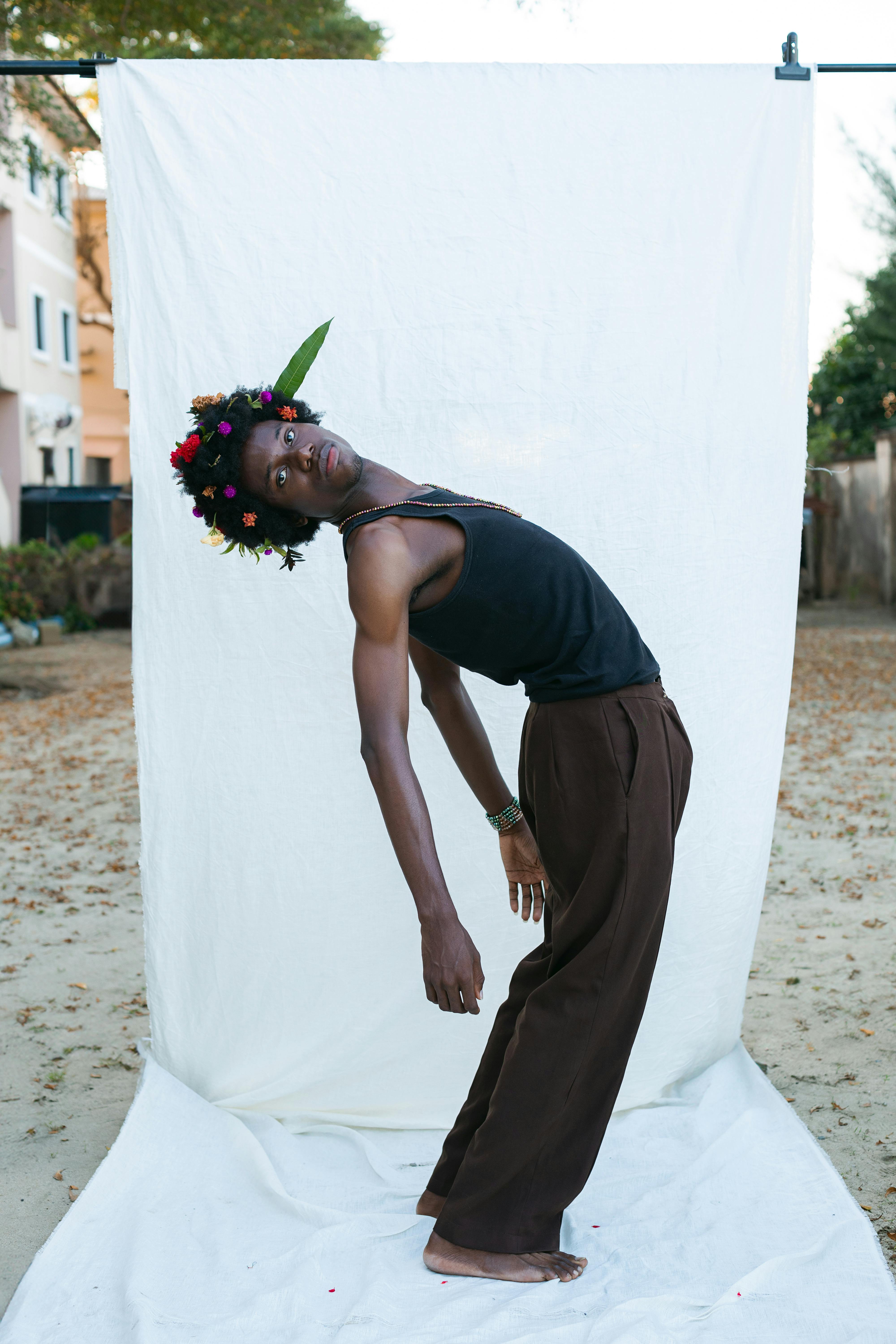 An expressive dancer poses outdoors, wearing a vibrant floral headpiece against a minimalist backdrop.