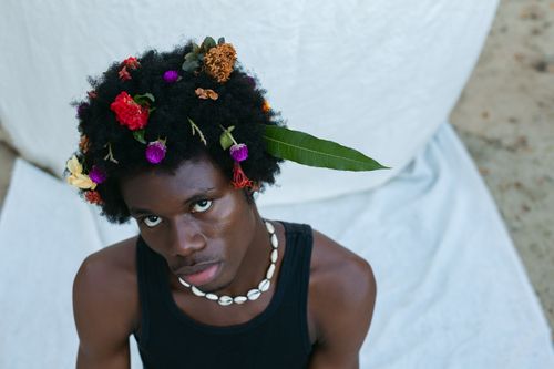 Gratis Ritratto creativo di un giovane con fiori nella sua acconciatura afro, che trasmette un'atmosfera vibrante. Foto a disposizione