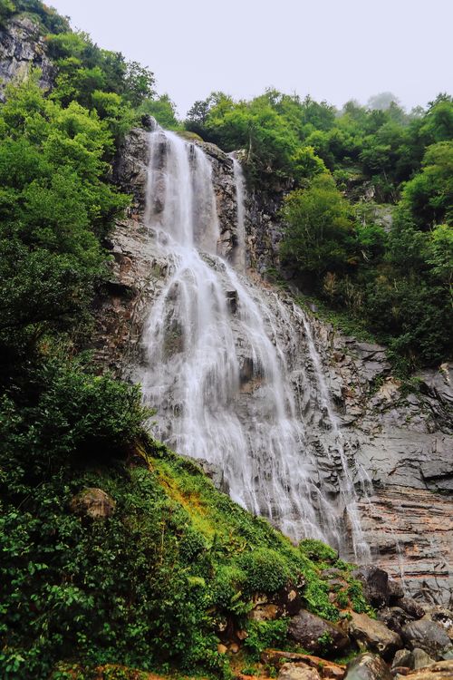 Free Stunning waterfall flowing down rocky cliffs surrounded by lush greenery in a serene forest setting. Stock Photo