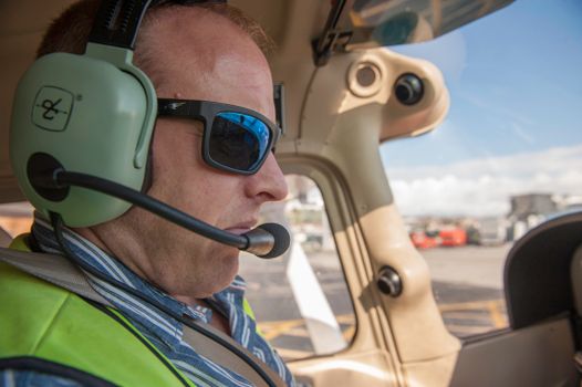 Photo by luis Peralta A pilot wearing sunglasses and a headset in the cockpit during a clear day.