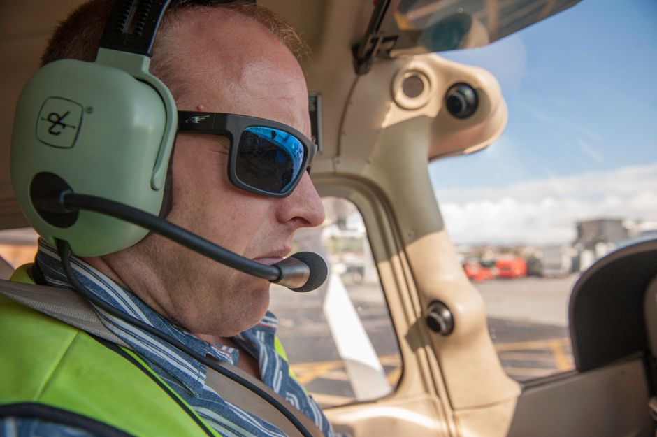 Photo by luis Peralta A pilot wearing sunglasses and a headset in the cockpit during a clear day.