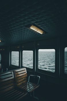 Dark and moody ferry interior showcasing ocean view through windows.