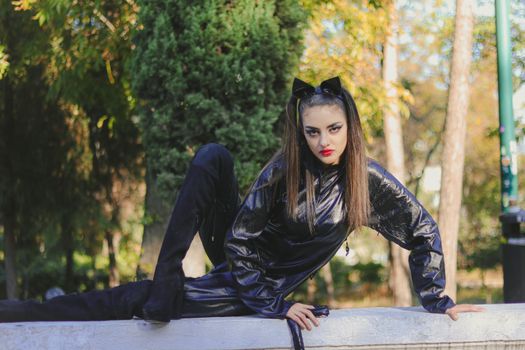 A woman in a black costume poses confidently outdoors, surrounded by autumn trees.