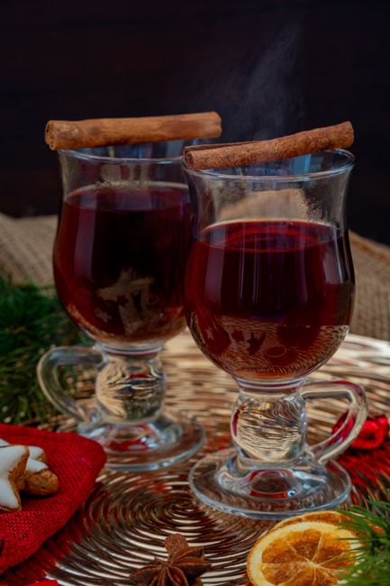 Two glass mugs of steaming mulled wine garnished with orange slices, cinnamon sticks, and star anise on a wooden table.
