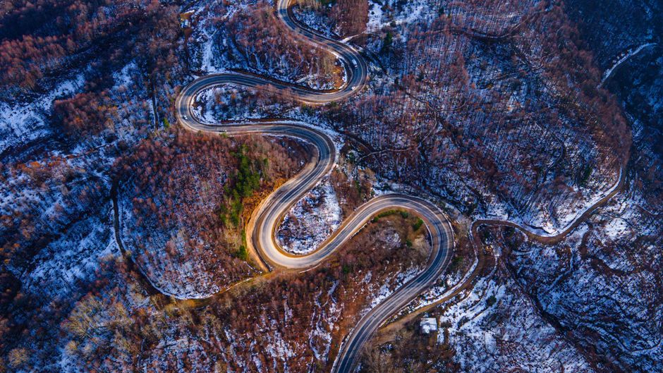 Sterk kronkelende bergweg gezien van bovenaf door een licht besneeuwd berglandschap