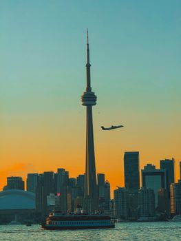 The Toronto skyline featuring the iconic CN Tower during a vibrant autumn sunset, with a plane flying overhead.