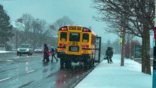 Free Kids boarding a yellow school bus in snowy winter conditions in a Canadian suburb. Stock Photo