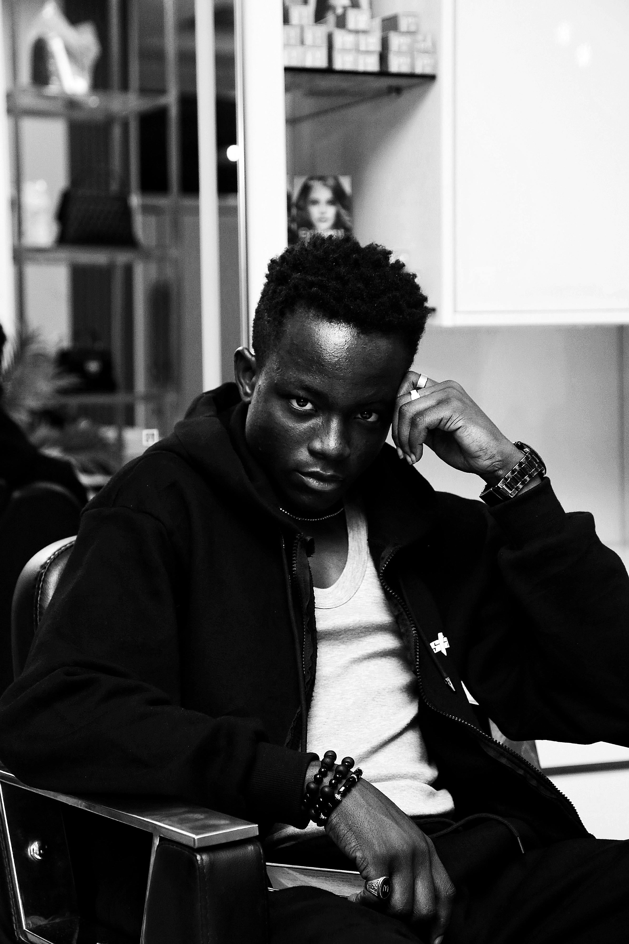 Black and white portrait of a young man sitting confidently in a modern hair salon.