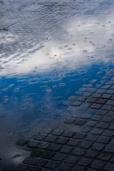 A serene image of a wet cobblestone street reflecting the sky and clouds.
