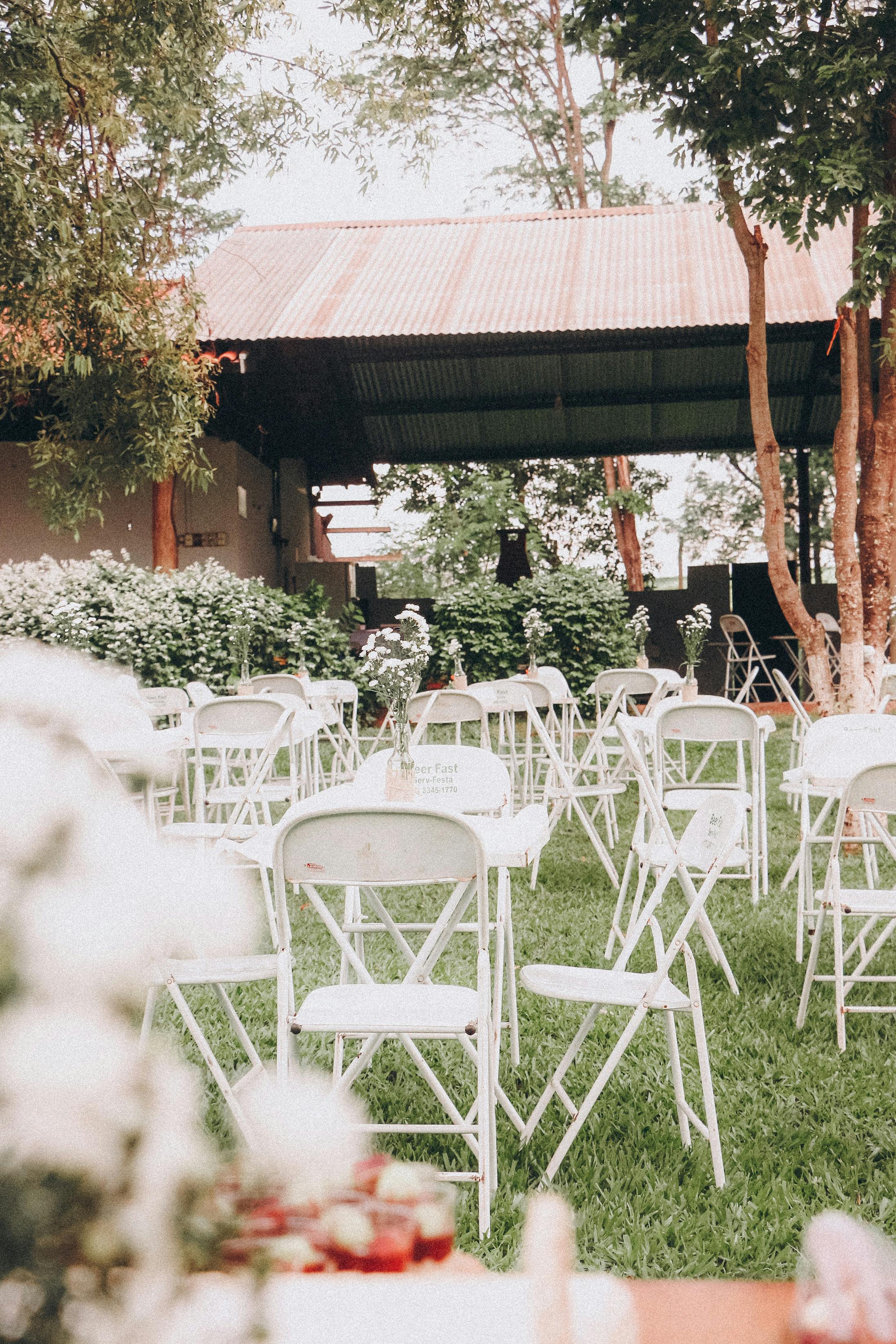 Elegant outdoor wedding setup with white chairs and floral decor on grassy lawn.