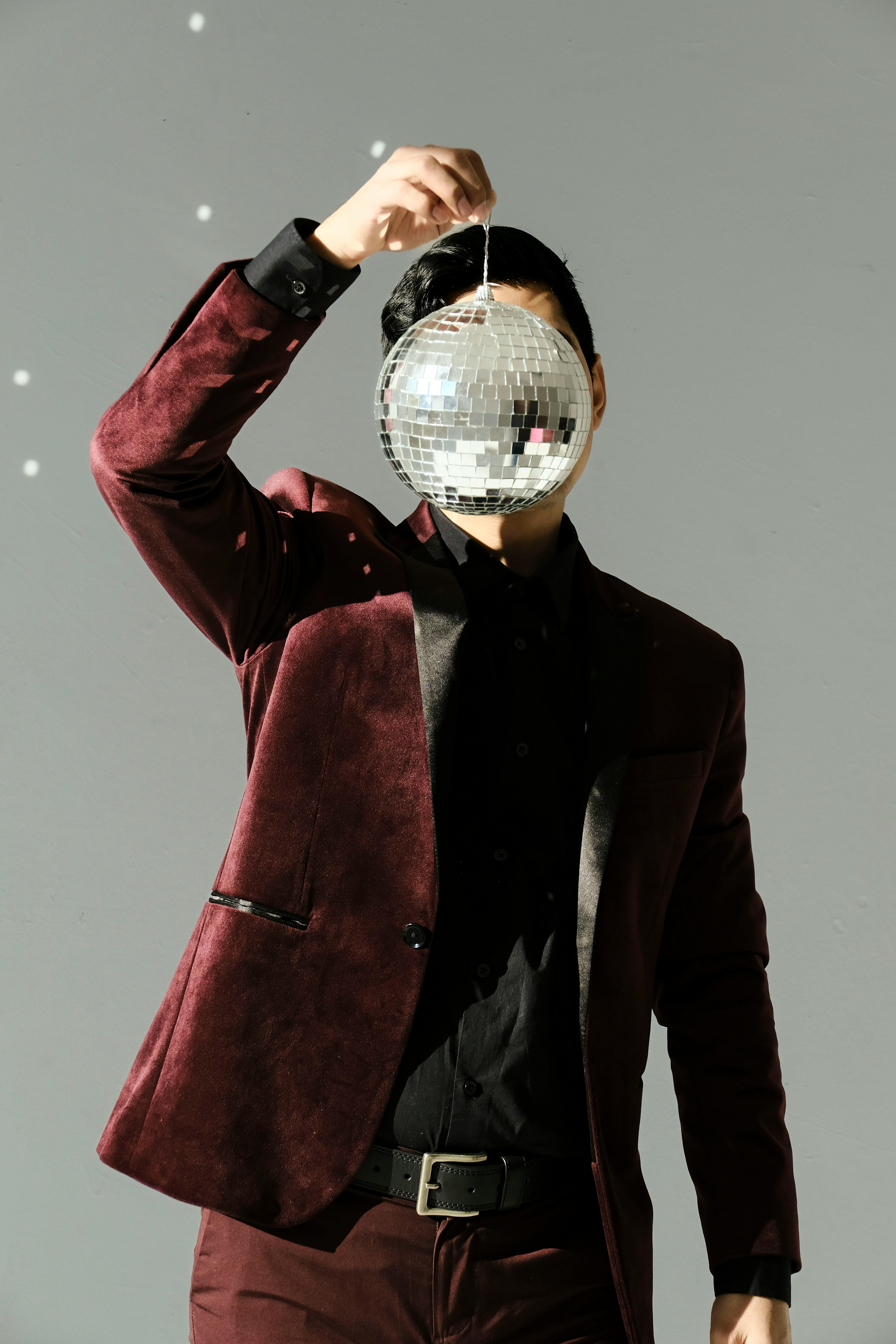무료 벨벳 정장을 입은 세련된 남자가 디스코 볼로 얼굴을 가렸다. 스톡 사진