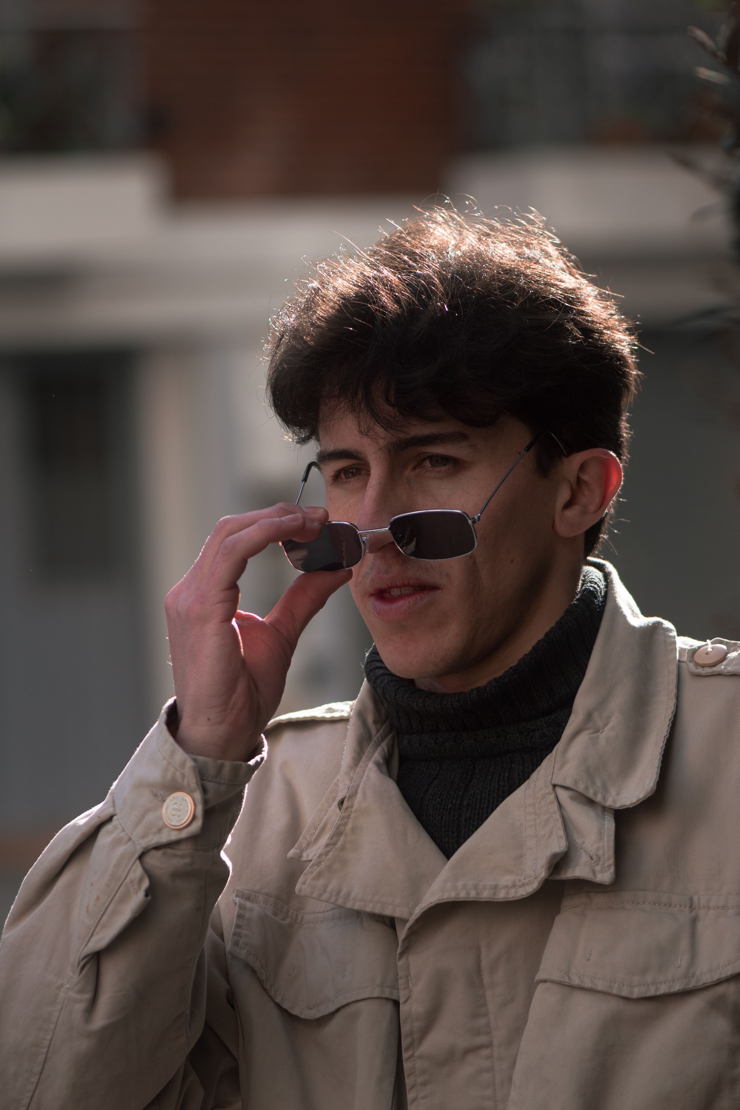 Stylish young man adjusting sunglasses in sunlight on Buenos Aires street.