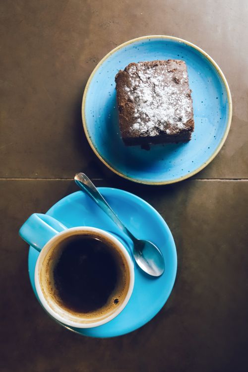 Free Top-down view of a coffee with a brownie dusted with powdered sugar on vibrant blue tableware. Stock Photo