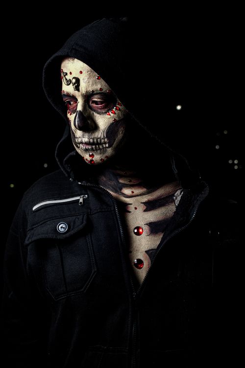 Free Striking portrait of a person with skull makeup and glowing eyes in a dark setting. Stock Photo
