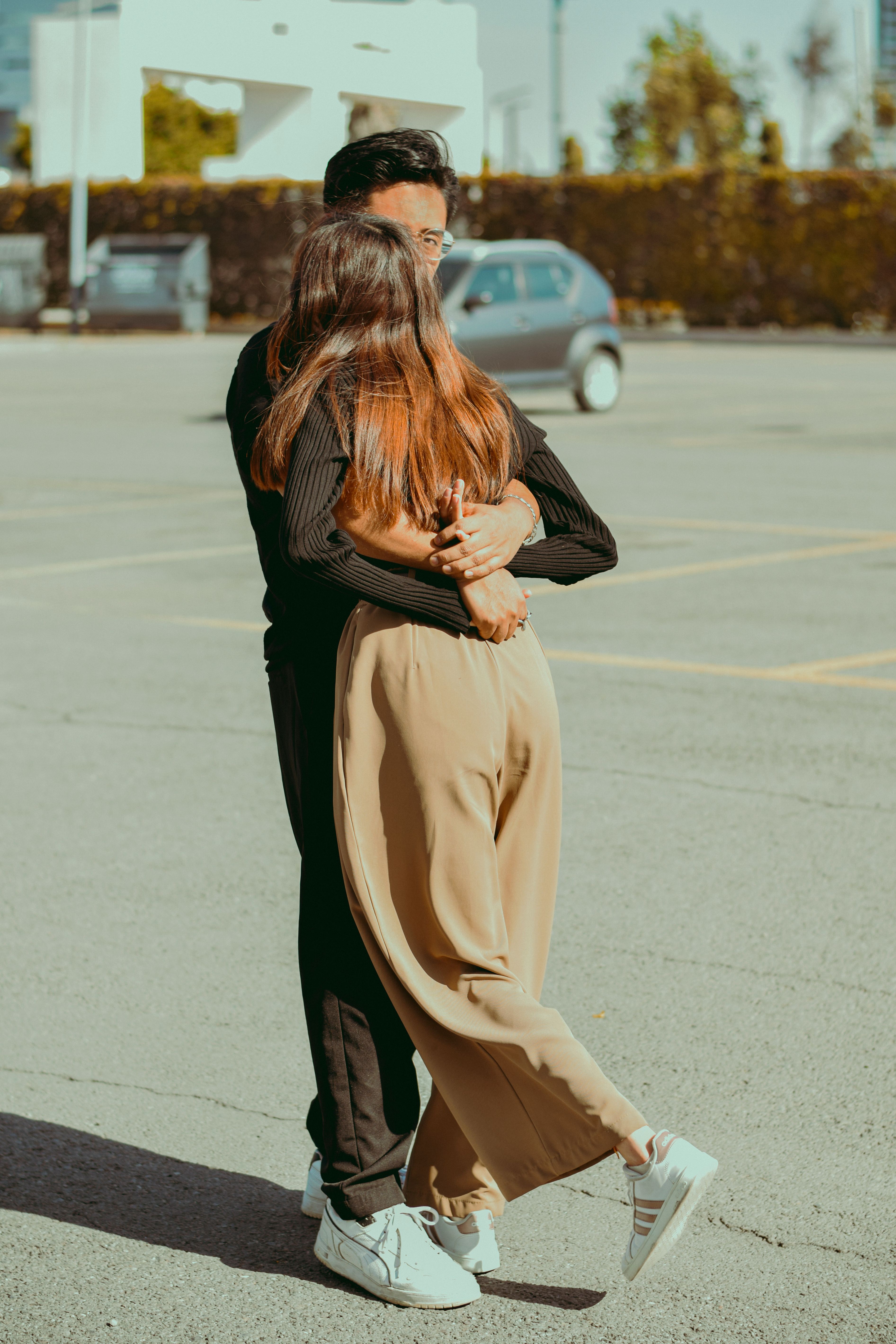 Fotomural Una pareja joven se abraza en un soleado aparcamiento urbano. Captura un momento tierno.