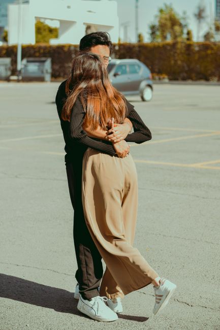 Fotomural Una pareja joven se abraza en un soleado aparcamiento urbano. Captura un momento tierno.