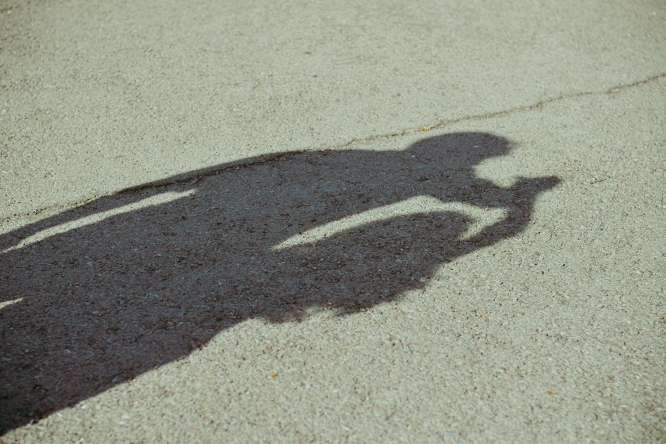 Sombra de uma pessoa segurando uma câmera refletida na superfície de uma calçada.