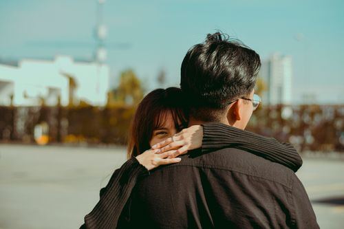 Free A woman playfully hugging a man outdoors in an urban setting, with a joyful smile. Stock Photo