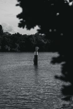 Black and white photo of a river with a navigation marker surrounded by trees.