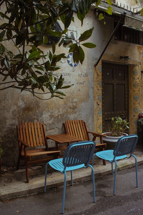 Free Outdoor seating with vintage wooden and blue chairs against an aged wall. Stock Photo