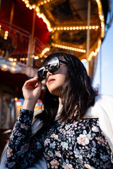 A woman in sunglasses poses confidently against a lively fairground backdrop.