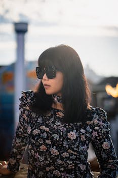 Fashionable woman in floral dress and sunglasses posing at dusk.