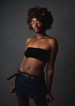 Artistic portrait of a young woman in denim skirt and tube top, with eyeglasses, conveying confidence.