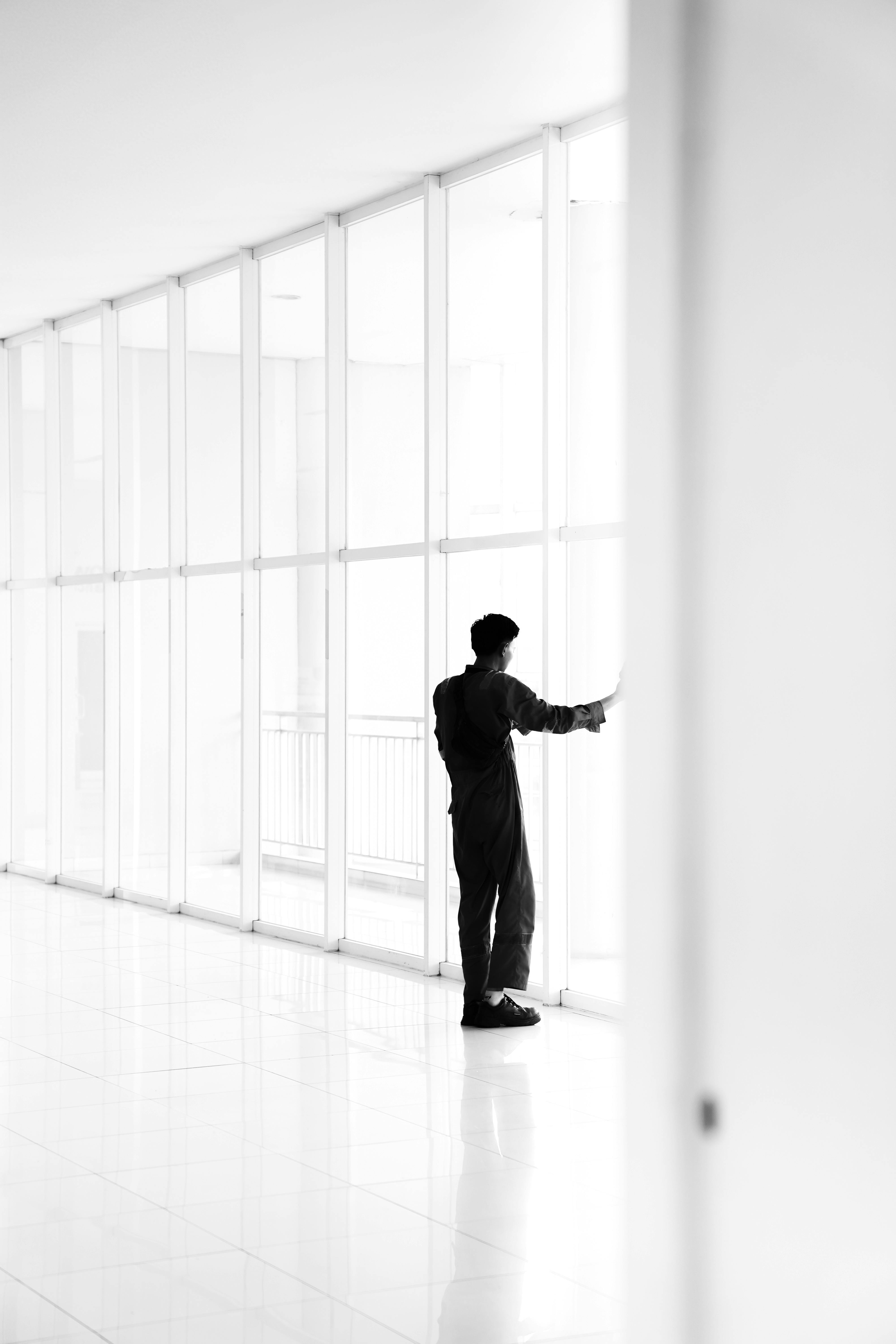 Silhouette of a person in a white corridor with floor-to-ceiling windows in a minimalist setting.