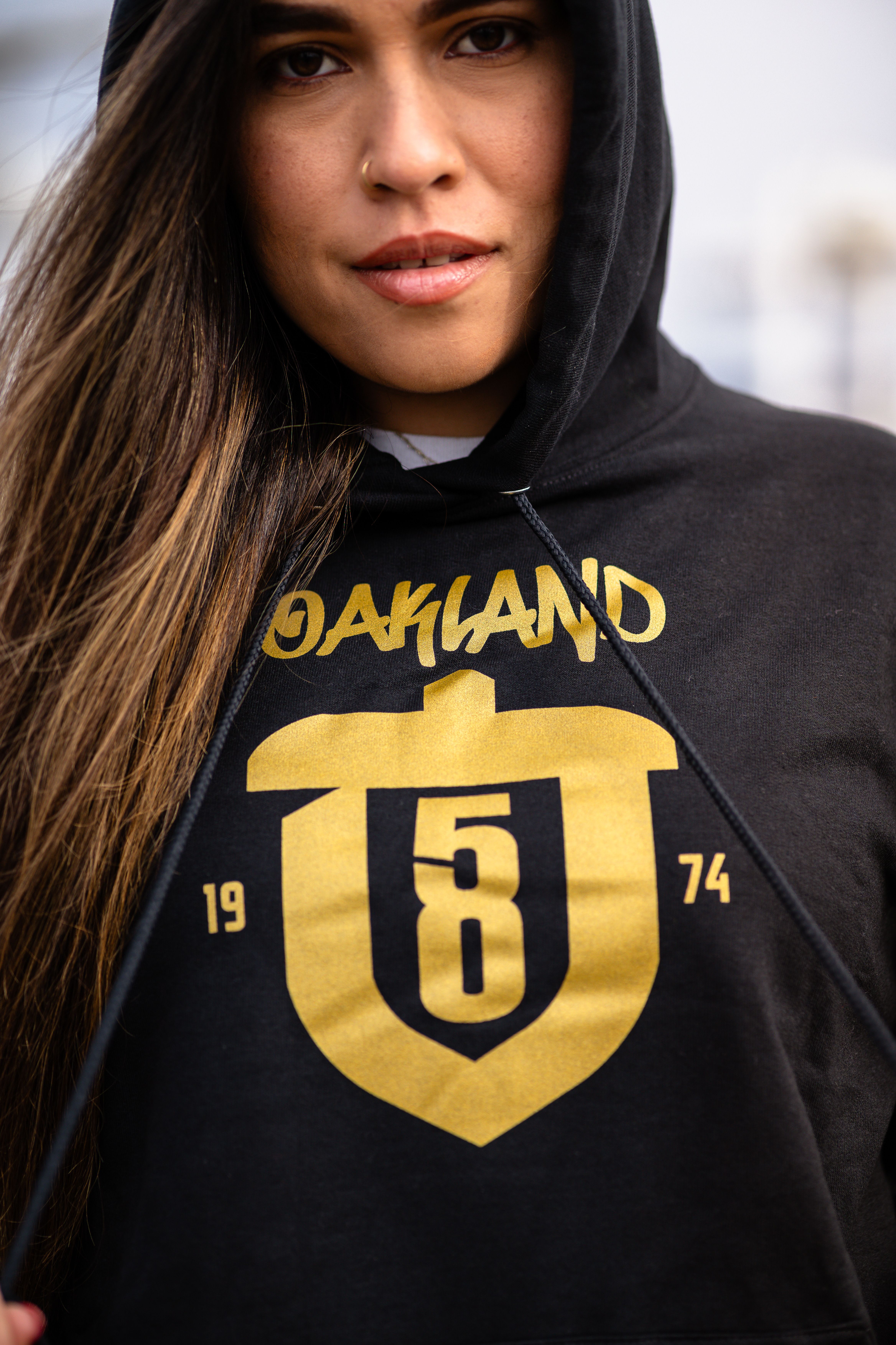 Close-up of a woman wearing a fashionable Oakland hoodie with gold emblem.