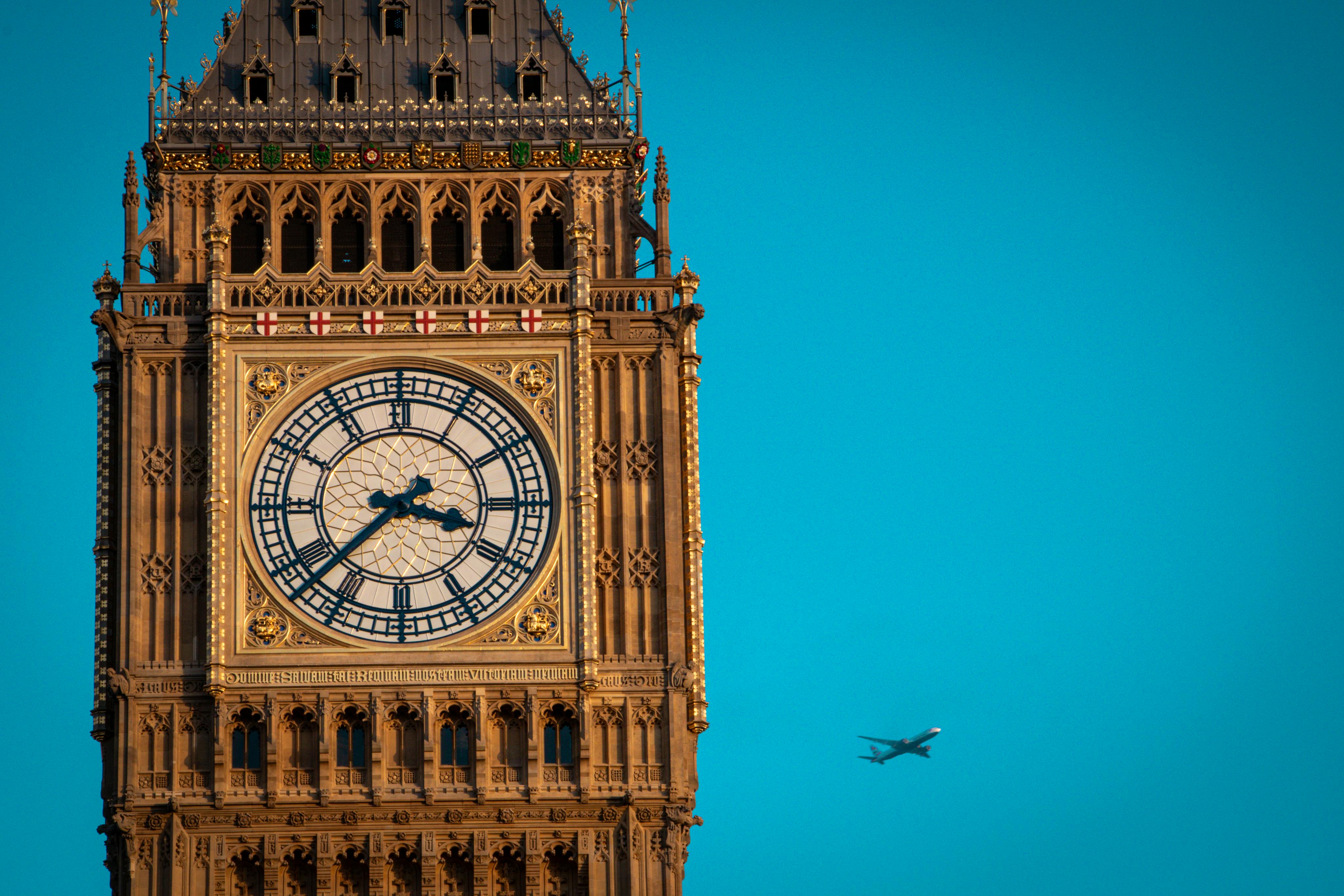 Iconic Big Ben clock tower in London with airplane flying by on a clear day. - Manchester