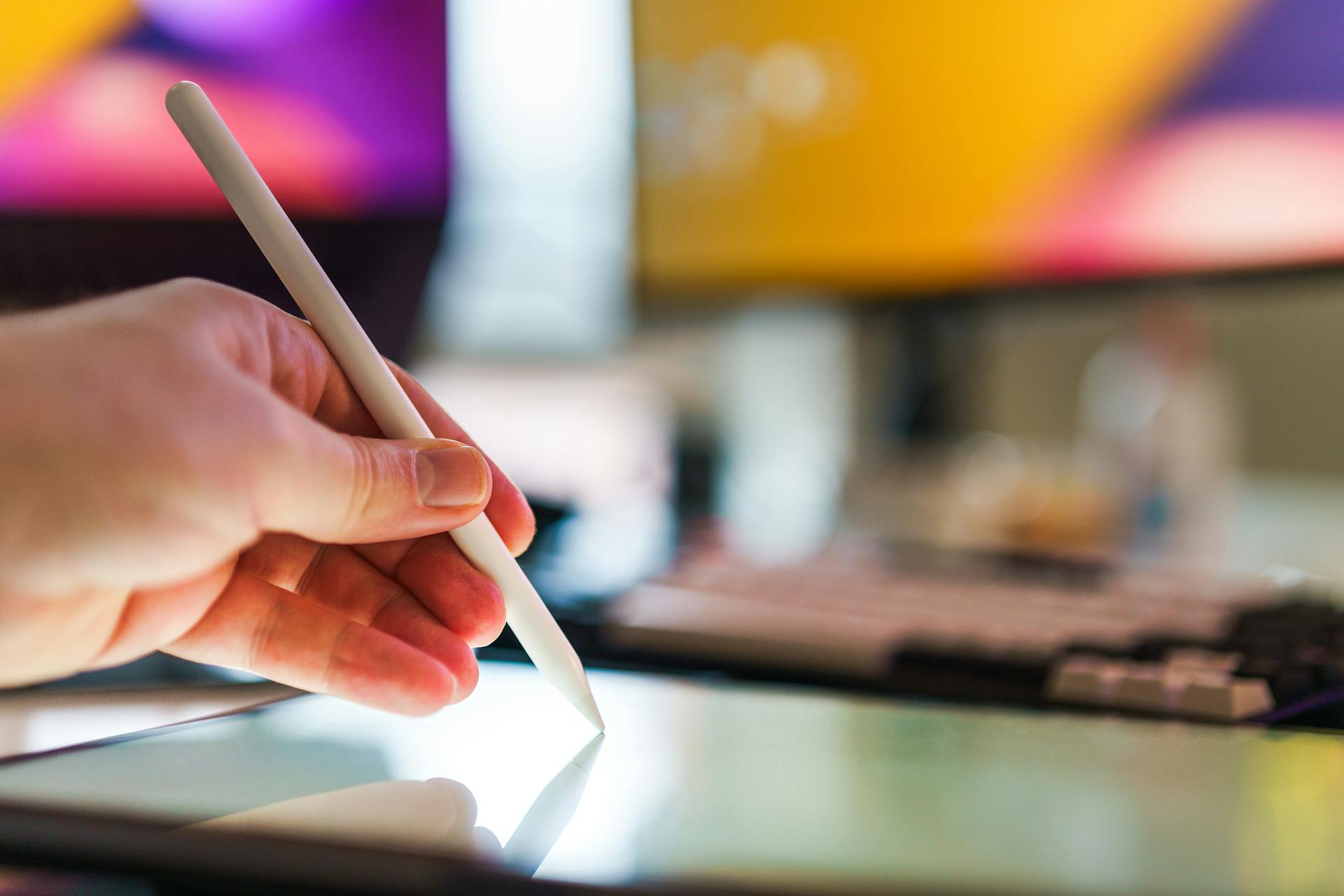 Close-up of a hand using a stylus on a digital tablet in a creative workspace.