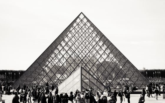 Monochrome foto van de Louvre-piramide met mensenmassa, een bezienswaardigheid in Parijs.