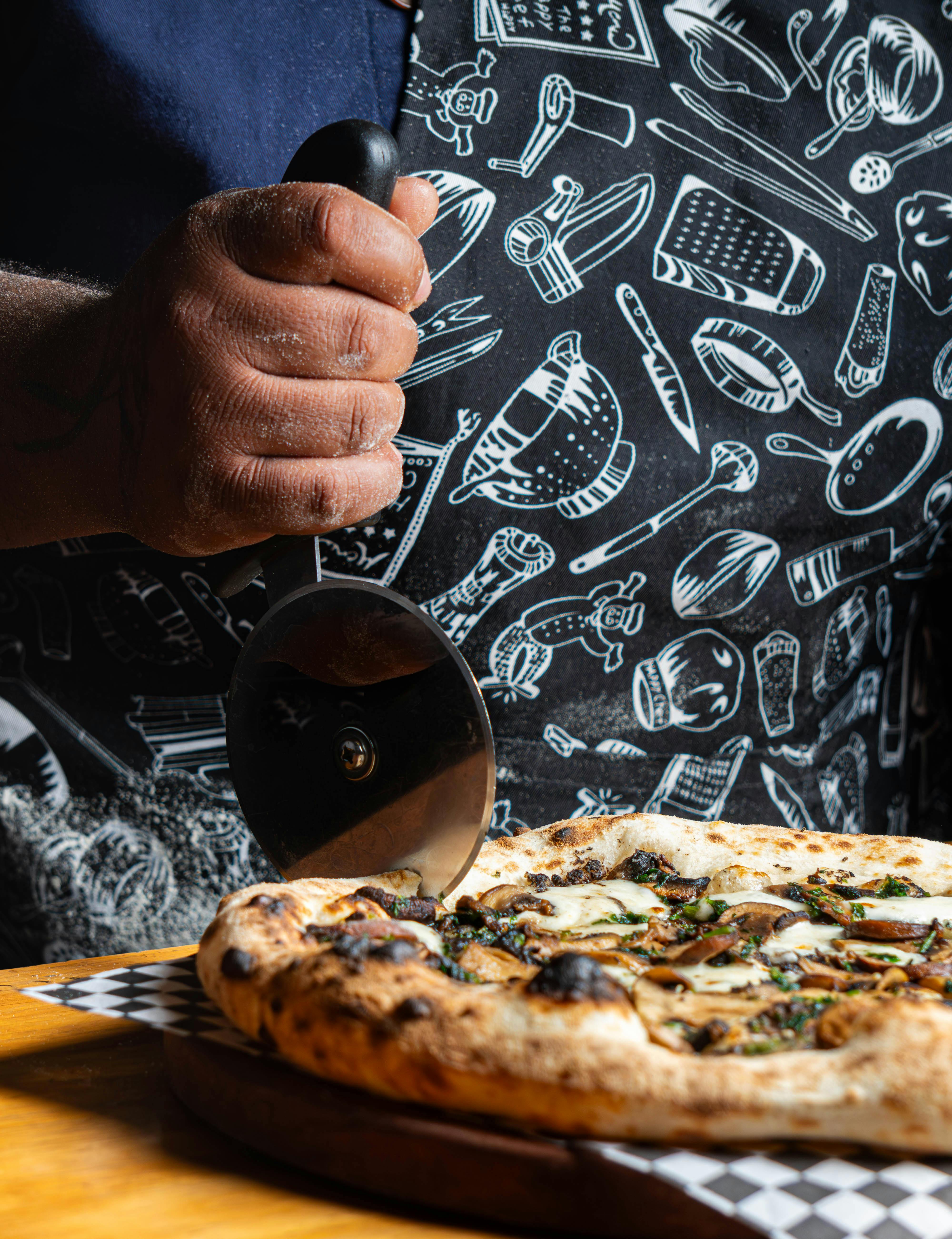 Close-up of a chef slicing a rustic gourmet pizza with a professional pizza cutter.