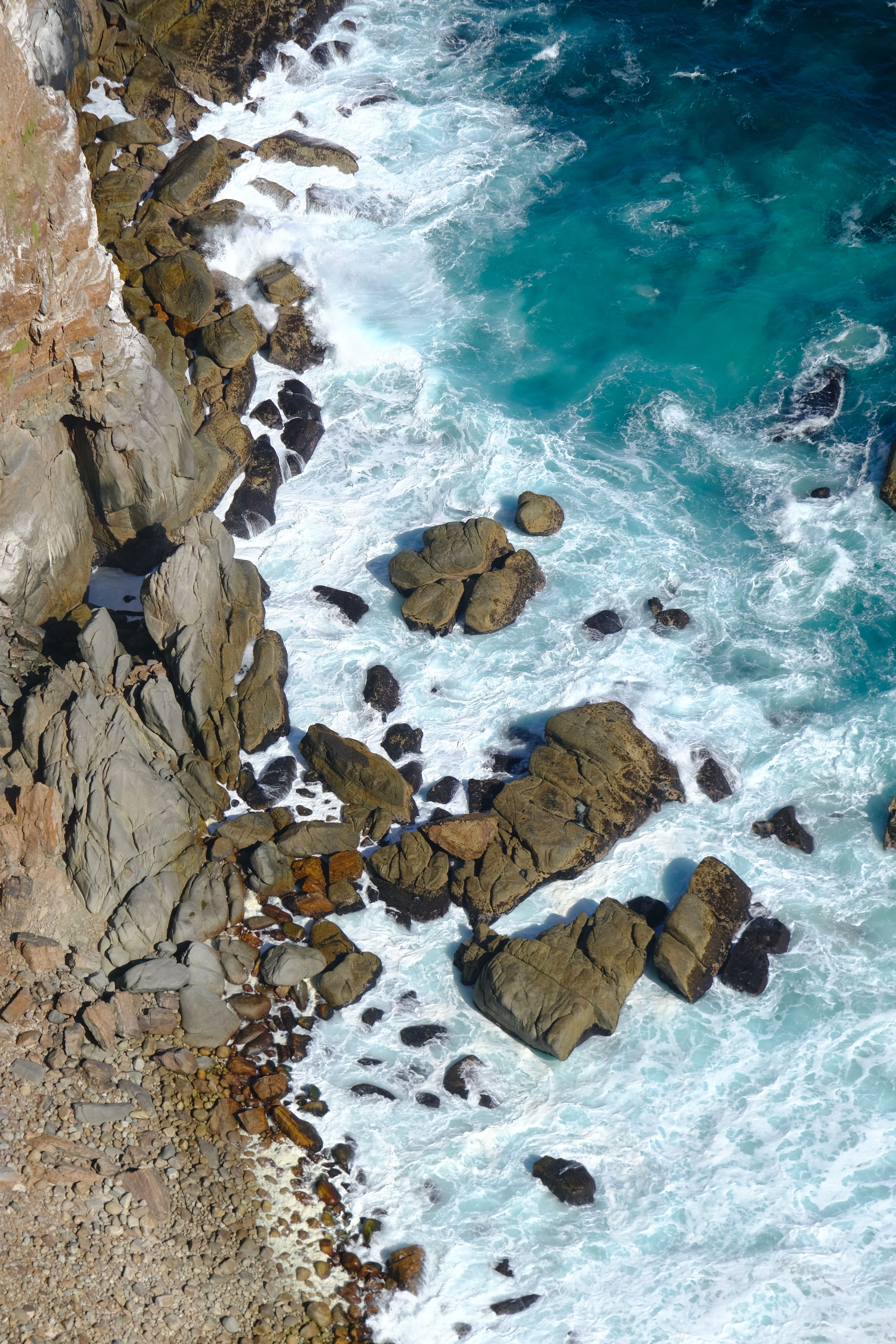 A stunning aerial shot of Cape Town's rocky coastline with crashing waves and vibrant blue waters.