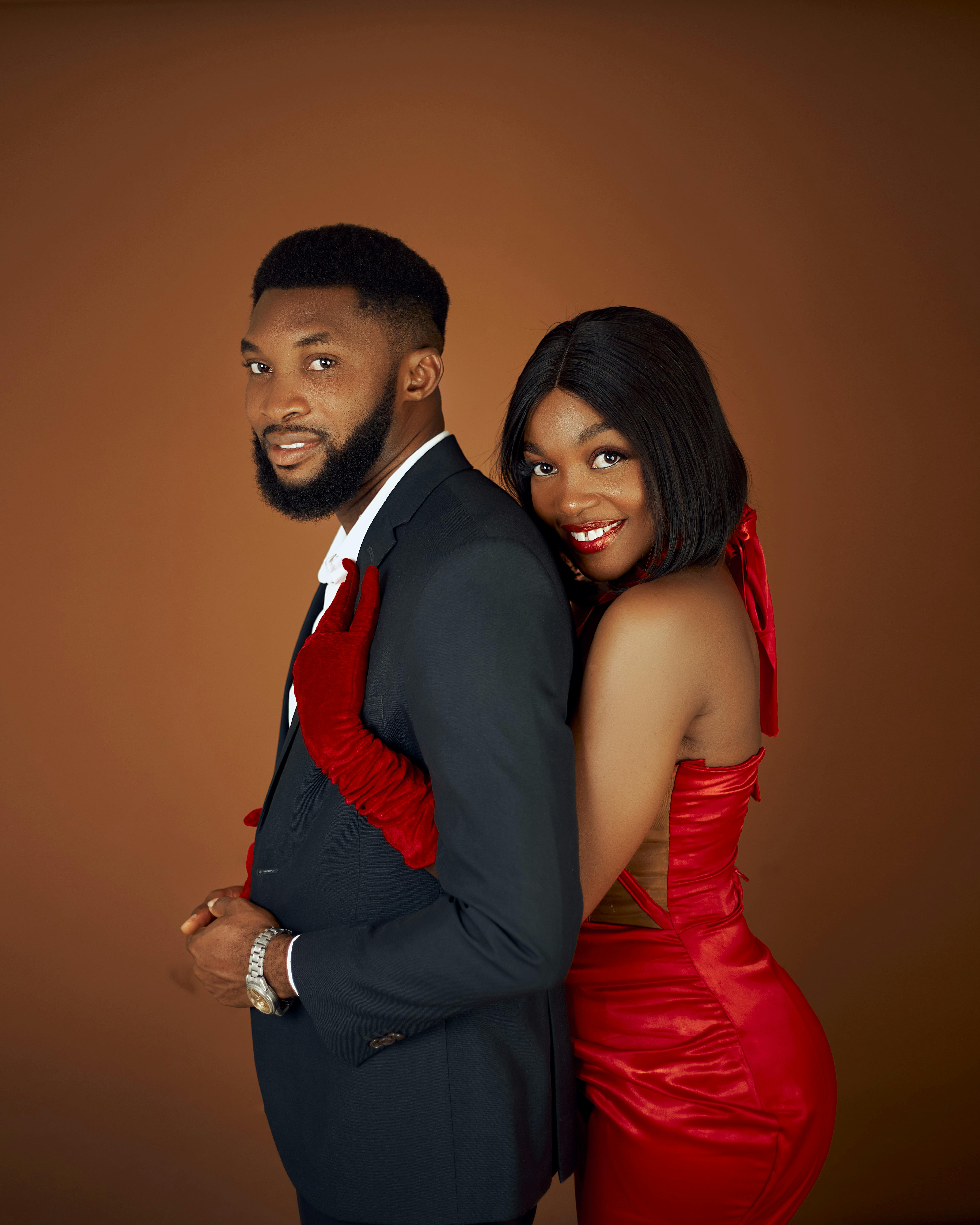 Elegant couple posing in a studio setting, showcasing formal wear with a warm backdrop and stylish attire.