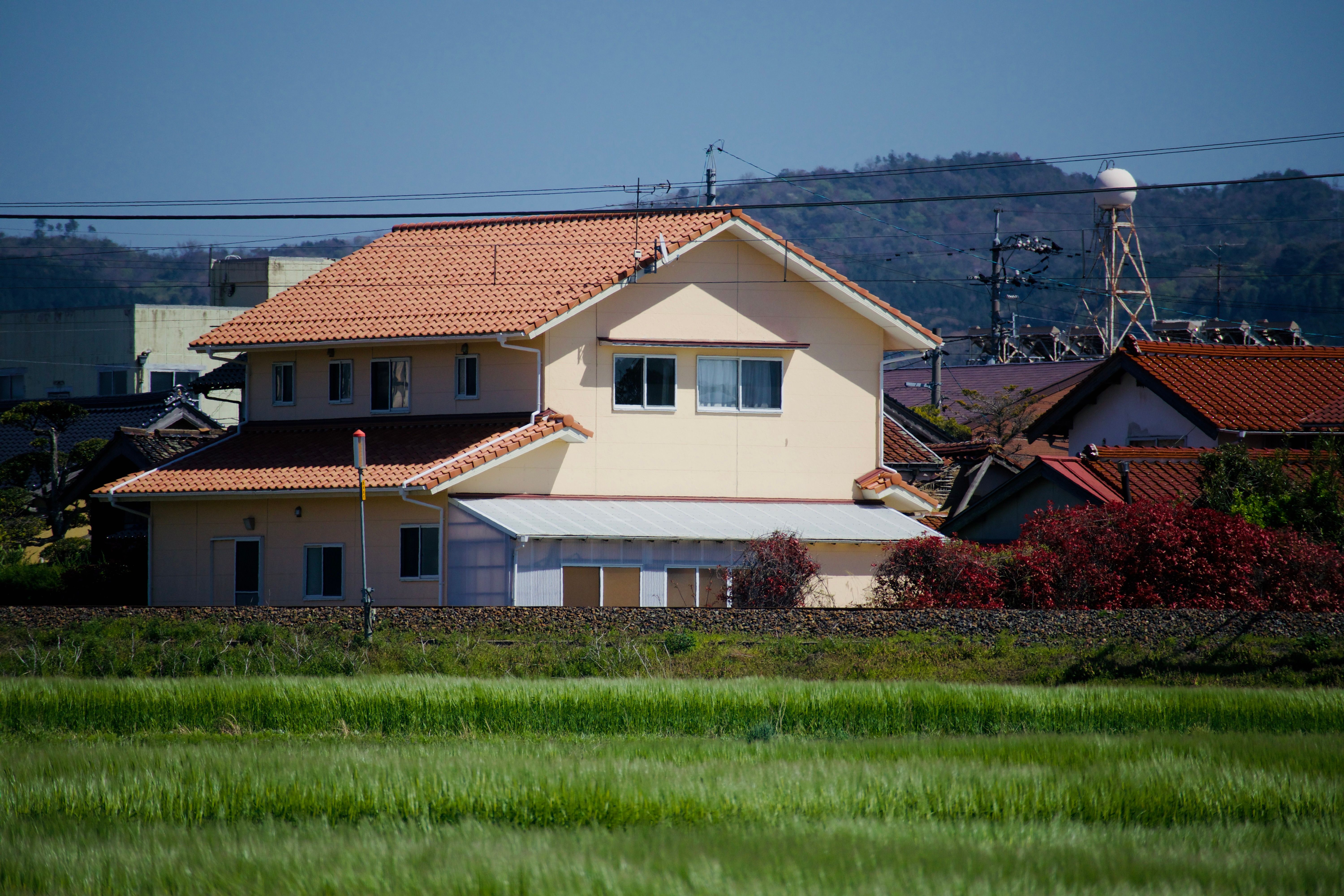 Une vue sereine sur la campagne avec une maison au toit de tuiles rouges entourée de verdure et de collines.