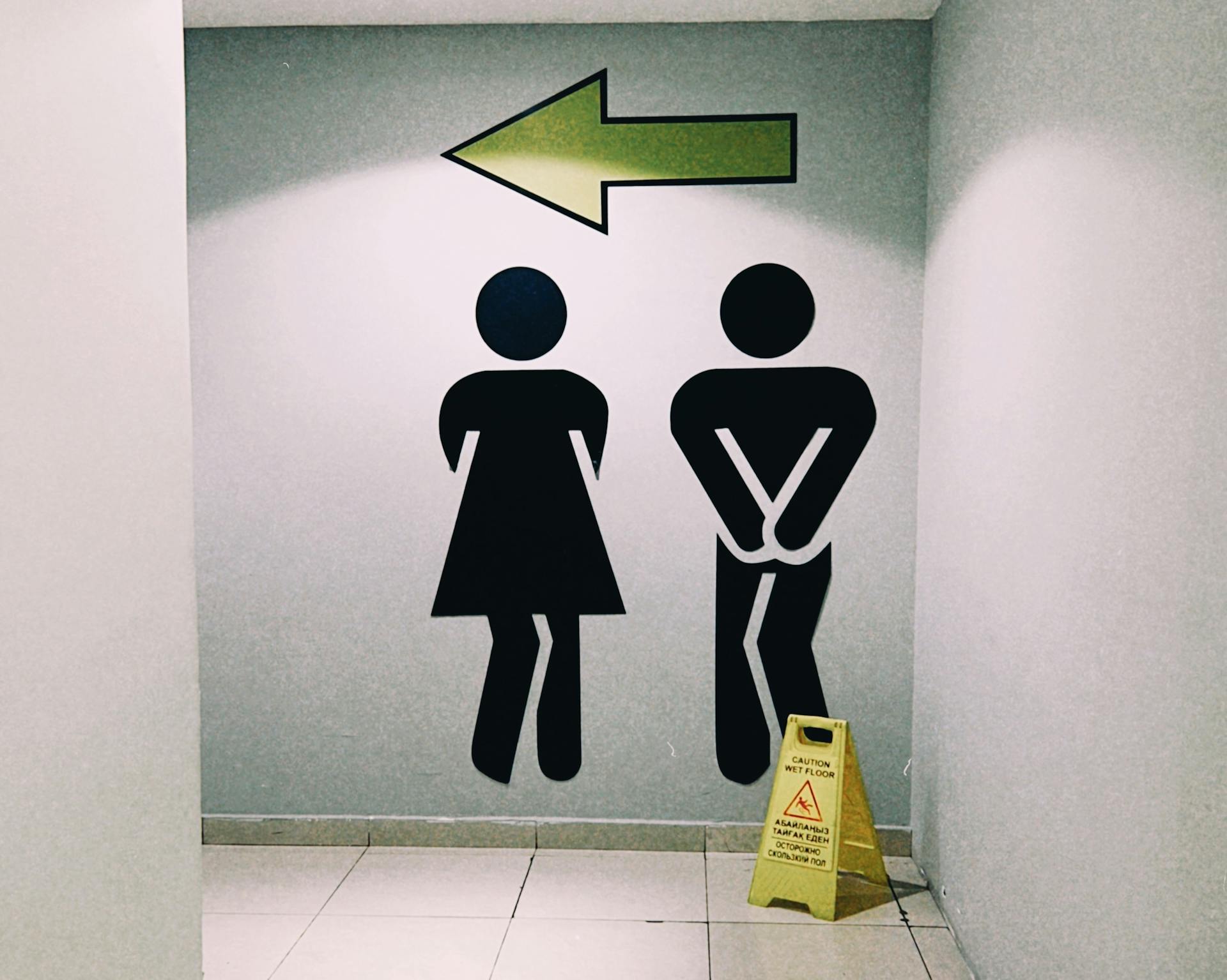 Modern restroom direction signage inside a mall in Almaty, Kazakhstan with wet floor caution sign.